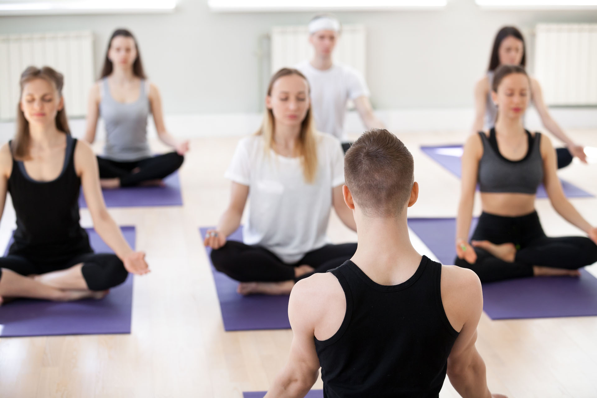 Group of sporty people doing Padmasana exercise with male instru